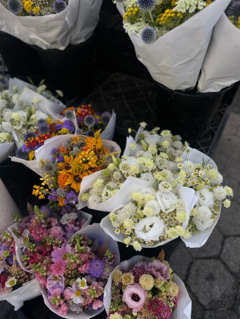 A collection of fresh flower bouquets arranged in white wrapping paper, featuring a variety of seasonal flowers including white roses, chrysanthemums, daisies, and vibrant blooms in shades of yellow, 