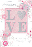 This image shows a romantic anniversary card designed in soft, harmonious tones that mirror the gentle character of Crofton Park's tree-lined streets. The central focus is the word LOVE, spelled out in tall, embossed letters that are generously dusted with fine, pale glitter. The texture looks slightly grainy and raised, inviting the fingers to wander across each letter as though tracing an intimate message. This sparkling word is placed on a central blush-pink panel, subtly deeper in colour than the rest of the card, adding a sense of depth and importance. Surrounding it, the background fades into a delicate wash of very light pink and creamy white, reminiscent of early morning sky above the railway arches. From the corners and edges, clusters of stylised flowers and foliage unfurl gracefully, as if gently growing across the surface. The blossoms and leaves are drawn with slim, flowing lines in shades of soft grey and white, while tiny touches of silver foil catch the light like dew on petals in a Crofton Park garden after rain. These floral illustrations drift around the central word rather than crowding it, leaving pockets of breathing space that keep the design calm and balanced. Curving stems and swirling flourishes add a sense of gentle movement, leading the eye in a circular path. Above and below the floral frame, an elegant, handwritten-style script conveys anniversary sentiments, the ink a discreet grey that sits lightly on the card. The overall impression is of tender, lasting love - like a pastel bouquet set on a windowsill overlooking Crofton Park - making this card feel like a keepsake as cherished as the occasion it marks.